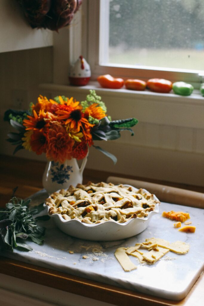 Photo of an unbaked pie on a marble board in the light of a window with flowers