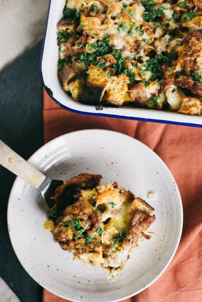 Photo of a slice of Sourdough Sausage Breakfast Strata on a small plate with the pan in the background