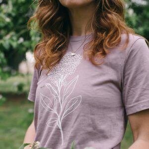 Image in a Potager Online Lilac Gardening Tee holding lilacs and wearing gardening gloves