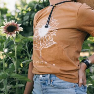 Photo of a woman wearing a Sunflower Gardening Tee standing in a potager garden with summer flowers