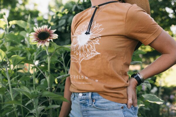 Photo of a woman wearing a Sunflower Gardening Tee standing in a potager garden with summer flowers