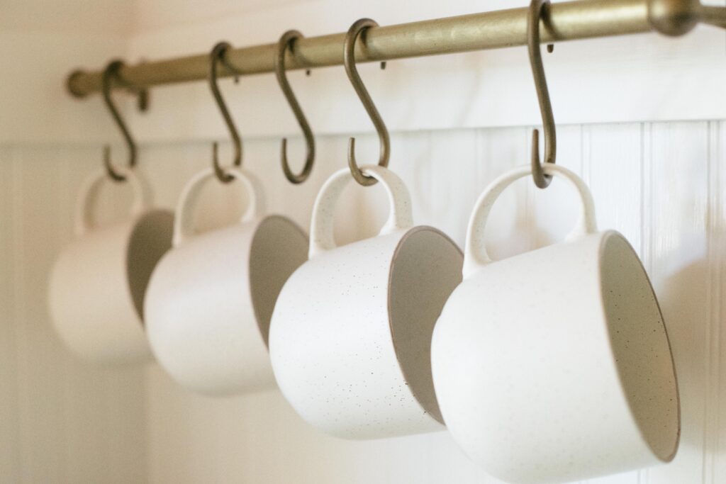 Image of a deVol brass pot rack with white stoneware mugs in an unfitted kitchen