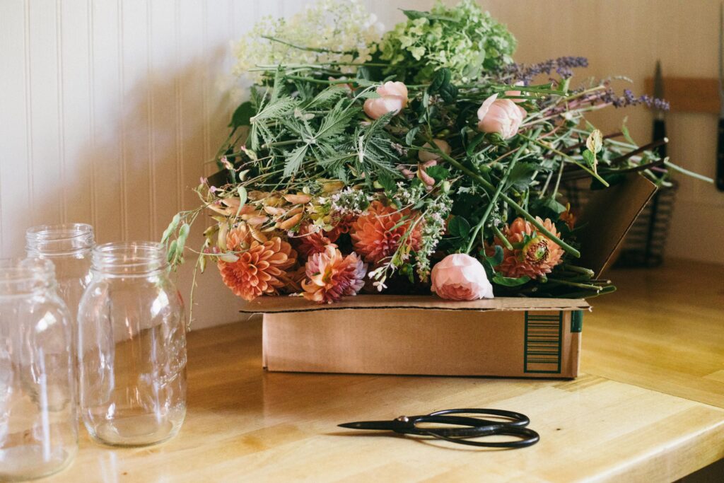 Cardboard box of garden flowers on a butcher block counter with mason jars and floral shears