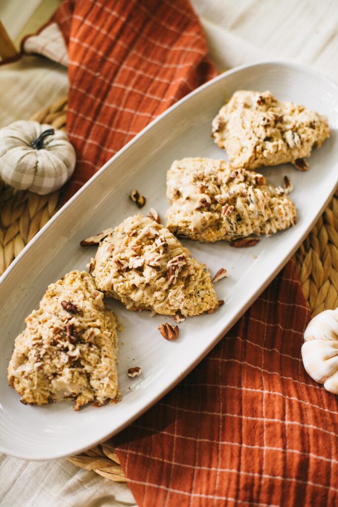 Image of einkorn maple pecan scones on a white platter on a burnt orange tablecloth with gingham pumpkins