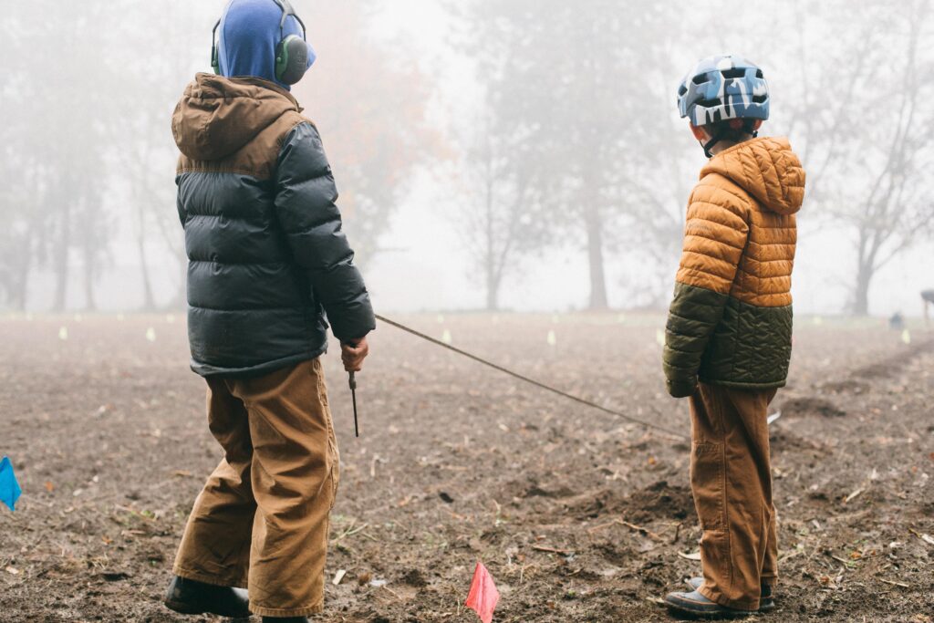 Two boys laying out a christmas tree farm row with a tape measure on on a homestead