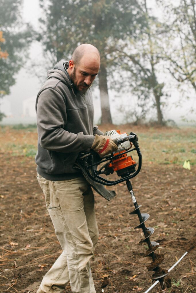 Image of a man with a hand held auger digging holes on his homestead for planting Christmas Trees