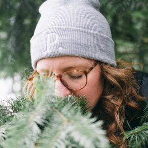 Image of a woman in a gray Potager Online beanie smelling Evergreen boughs