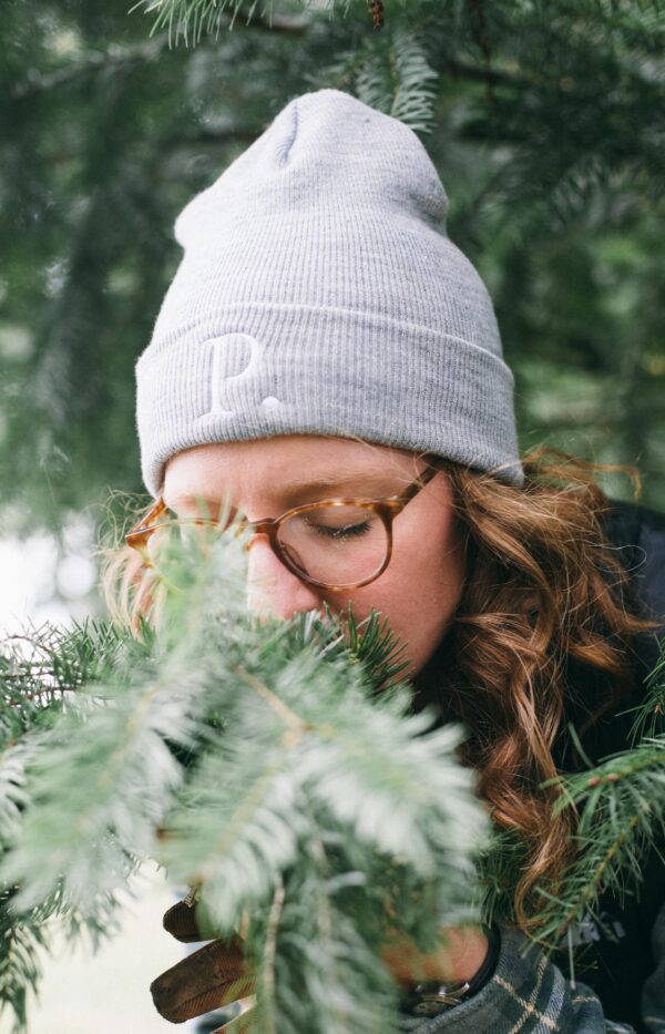 Image of a woman in a gray Potager Online beanie smelling Evergreen boughs