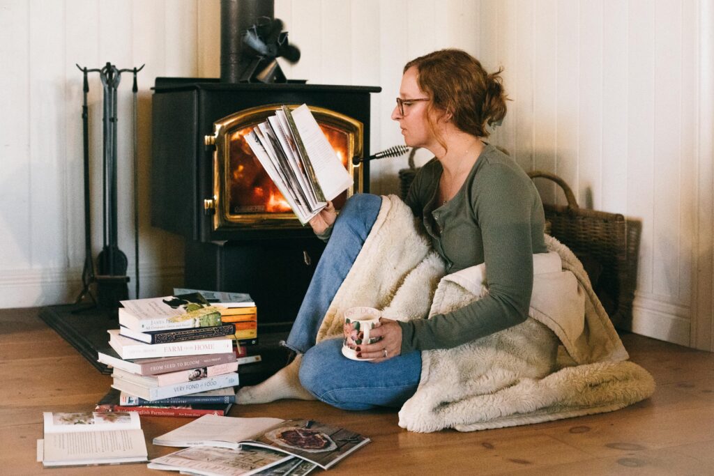 Image of a woman sitting in front of a wood stove reading books during the Winter