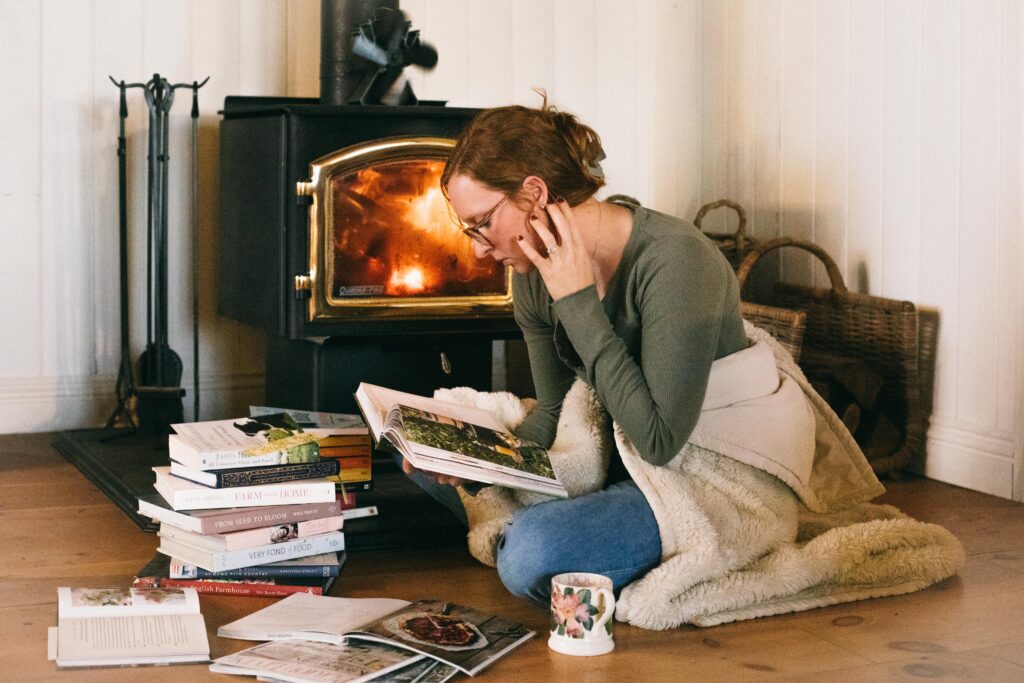 Image of a woman sitting in front of a wood stove reading books during the Winter