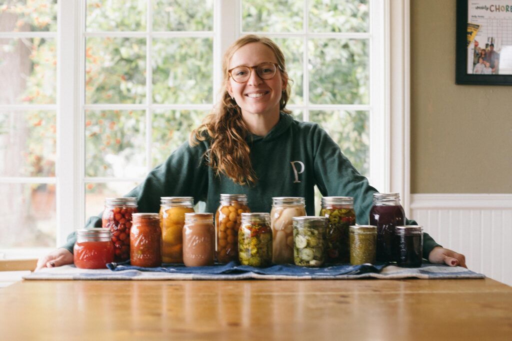 Image of a woman with a variety of canning goods from the garden